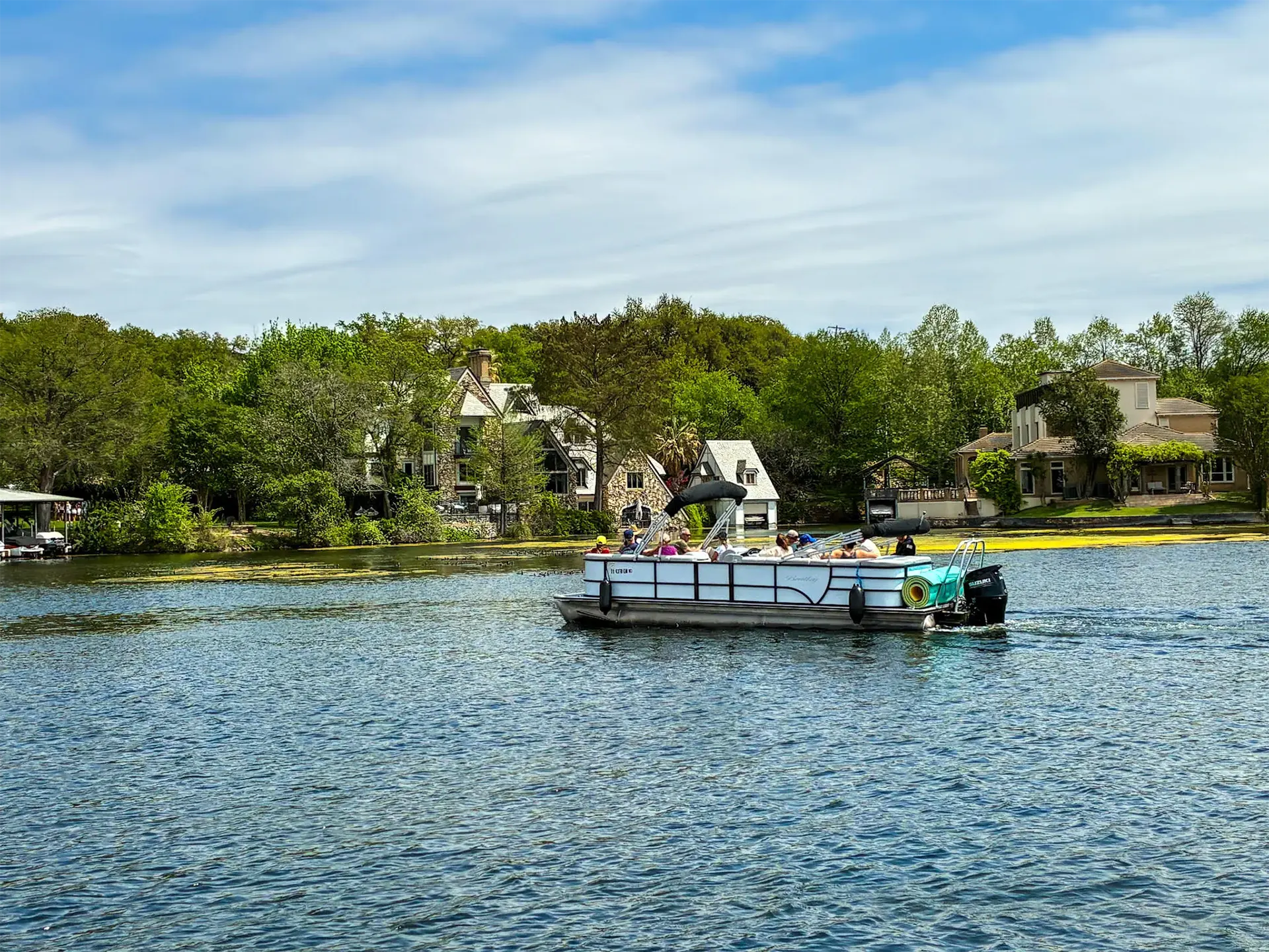 Private pontoon boat cruising past waterfront homes on Lake Austin